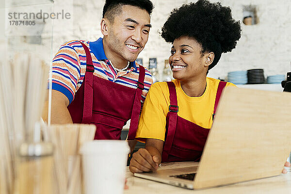 Lächelnder junger Mann und Frau  die Laptop im Café teilen