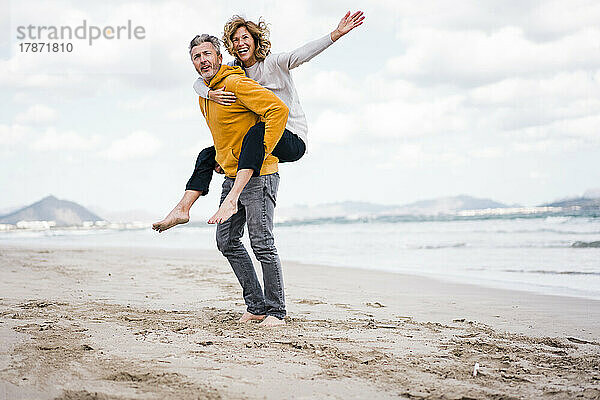 Reifer Mann und Frau genießen Huckepackfahrt am Strand