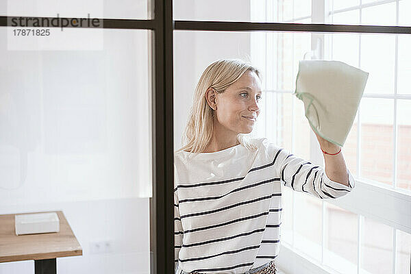 Lächelnde Frau reinigt Glaswand zu Hause