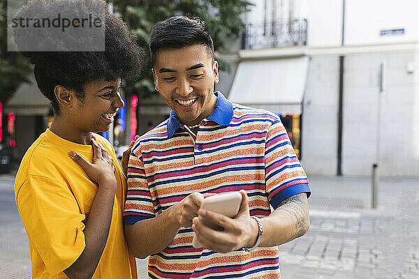 Fröhliche junge Frau schaut Mann mit Smartphone an