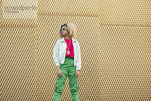 Frau mit Afro-Frisur und Sonnenbrille steht vor der Wand