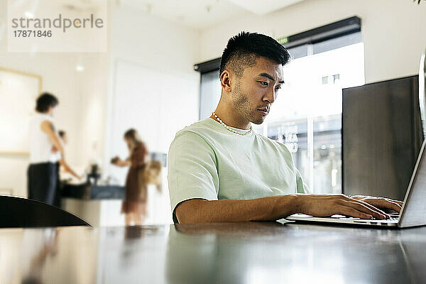 Junger Mann sitzt mit Laptop am Tisch im Café