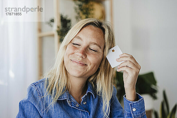 Lächelnde Frau mit geschlossenen Augen und Kreditkarte in der Hand