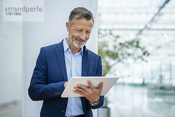 Lächelnder reifer Geschäftsmann mit digitalem Tablet vor der Säule