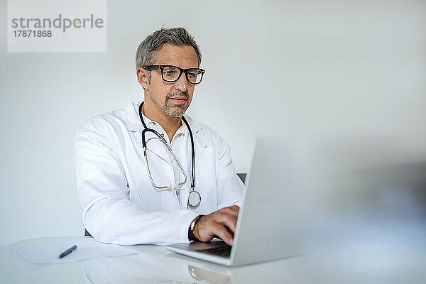 Reifer Arzt benutzt Laptop am Schreibtisch in der Arztpraxis