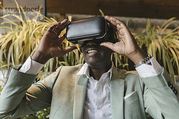 Glücklicher Geschäftsmann mit Virtual-Reality-Simulator im Café