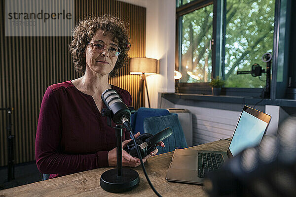 Reifer Moderator mit Brille und Headset sitzt mit Laptop am Schreibtisch im Radiosender