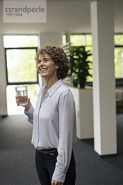 Glückliche Geschäftsfrau steht mit einem Glas Wasser im Büro