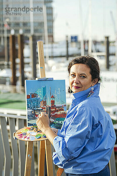 Lächelnder Künstler mit Palettenmalerei am Hafen