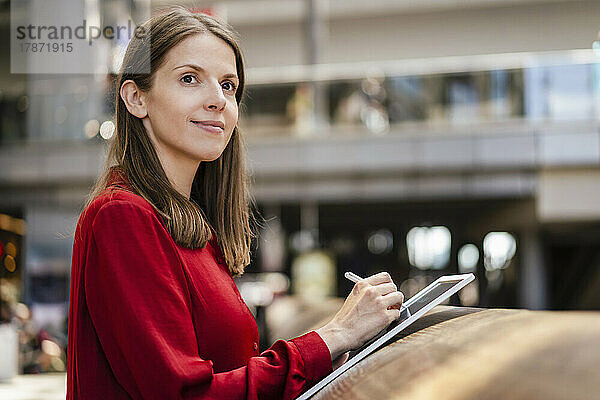 Nachdenkliche Geschäftsfrau mit digitalisiertem Stift und Tablet-PC am Arbeitsplatz