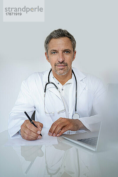 Porträt eines reifen Arztes  der in einer Arztpraxis am Schreibtisch sitzt