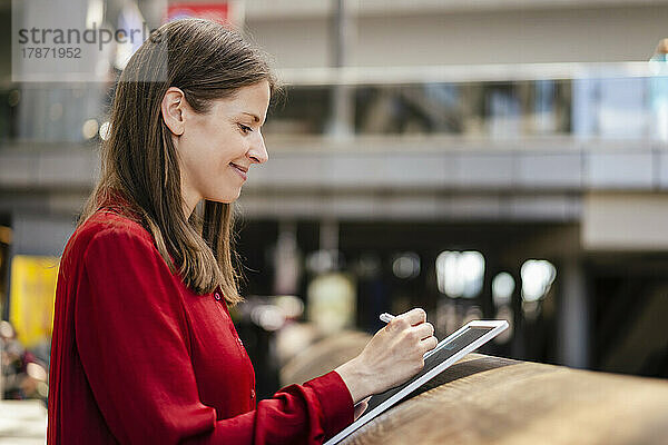 Lächelnde Geschäftsfrau  die am Arbeitsplatz einen digitalisierten Stift auf einem Tablet-PC verwendet