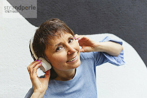 Lächelnde reife Frau  die mit Kopfhörern Musik hört