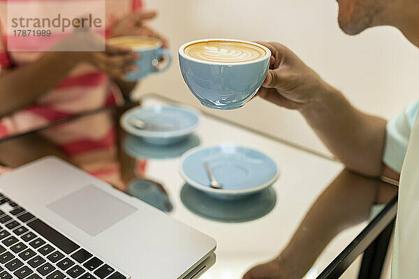 Mann und Frau halten Cappuccino-Tassen am Tisch im Café