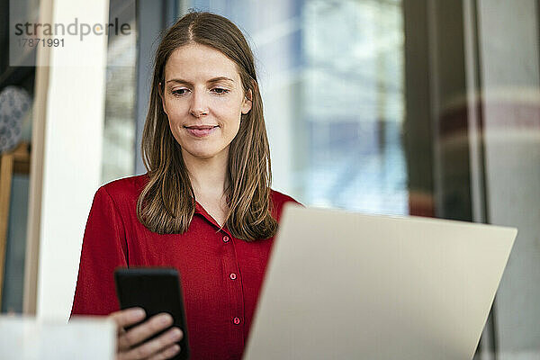 Geschäftsfrau nutzt Mobiltelefon per Laptop im Büro