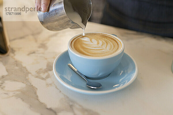 Hand eines Baristas  der Schaumkunst in einer Kaffeetasse herstellt