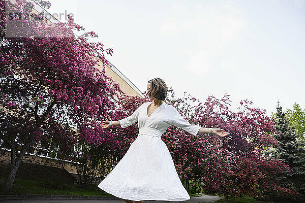 Frau in weißem Kleid mit ausgestreckten Armen im Apfelblütengarten