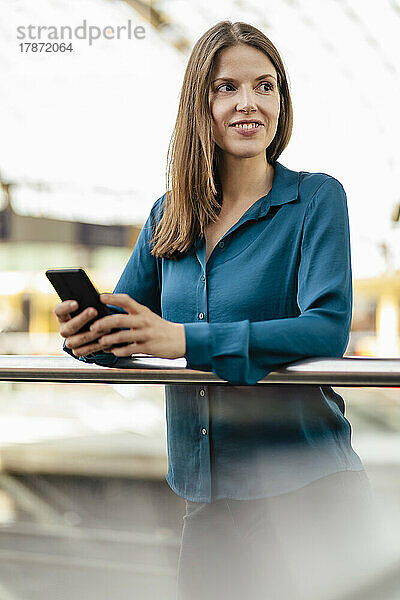 Lächelnde Geschäftsfrau mit Smartphone im Büroflur