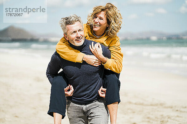 Glücklicher Mann gibt einer Frau am Strand an einem sonnigen Tag eine Huckepackfahrt