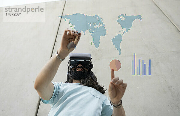 Lächelnder bärtiger Mann mit VR-Brille  der Karten und Diagramme berührt