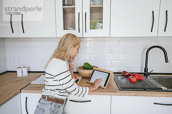 Junge Frau benutzt Tablet-PC auf der Küchentheke zu Hause