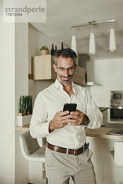 Lächelnder Geschäftsmann  der zu Hause sein Mobiltelefon benutzt