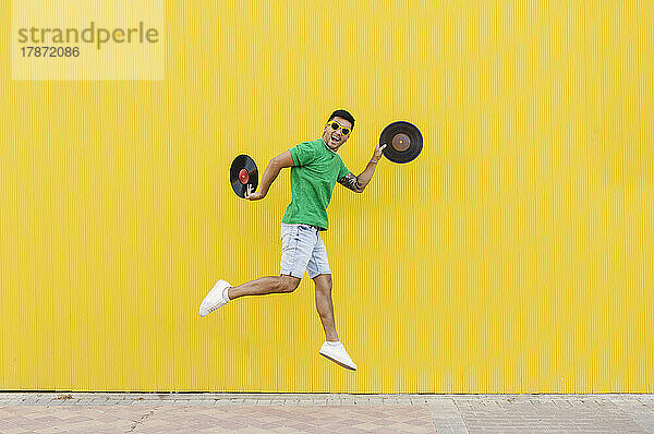 Young man jumping with vinyl records in front of wall