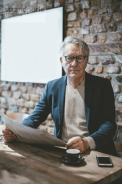 Überzeugter älterer Geschäftsmann mit Zeitung im Café