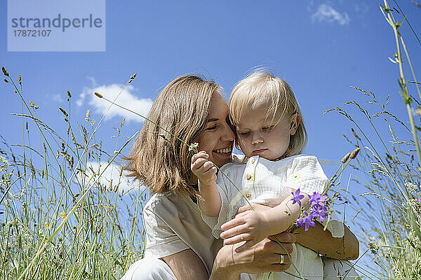 Smiling mother embracing cute daughter on field