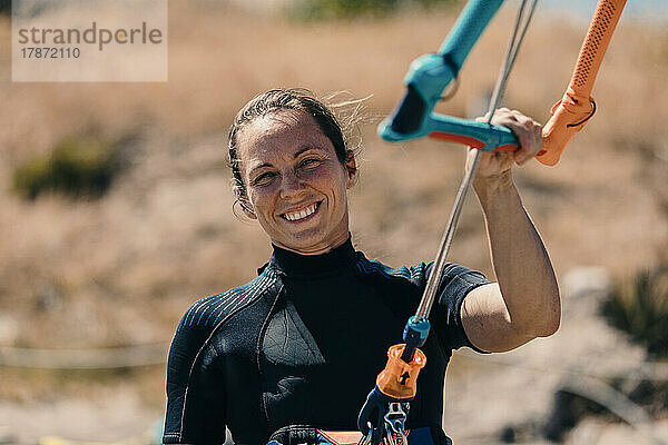 Lächelnde Frau beim Kitesurfen am Strand an einem sonnigen Tag