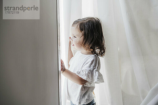 Cute little girl looking out of window at home