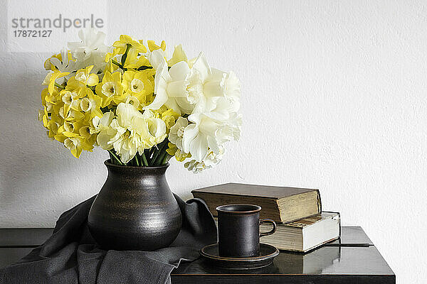 Studioaufnahme einer Vase mit blühenden Narzissen  die auf einem rustikalen Tisch steht