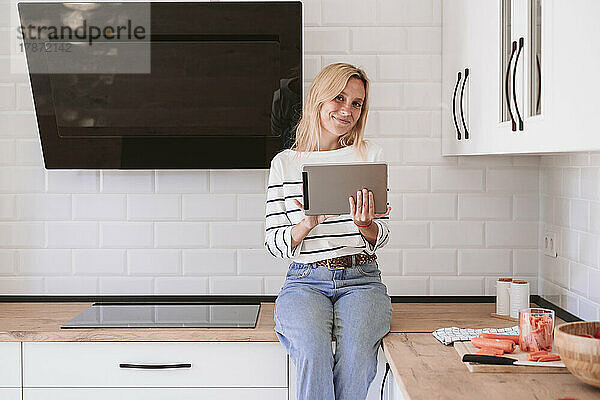 Lächelnde Frau mit Tablet-PC auf der Küchentheke zu Hause