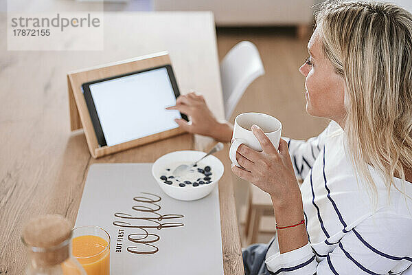 Junge Frau benutzt Tablet-PC und trinkt zu Hause Kaffee