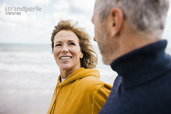 Glückliche reife Frau mit Mann  der am Strand spaziert