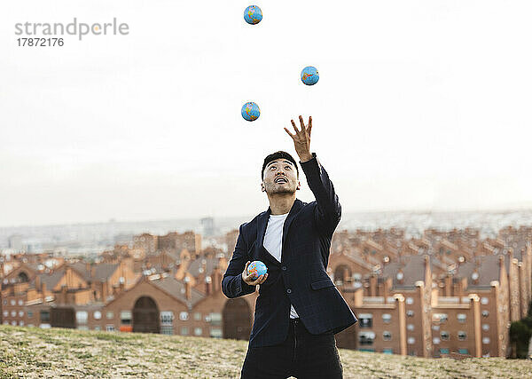 Junger Geschäftsmann jongliert mit Globen auf einem Hügel
