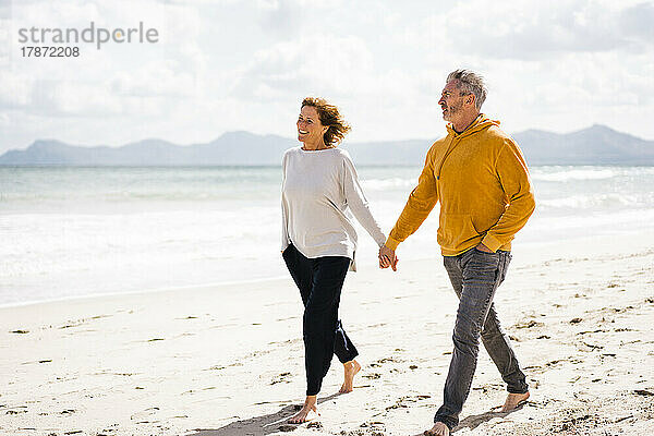 Happy couple holding hands walking at shore on sunny day