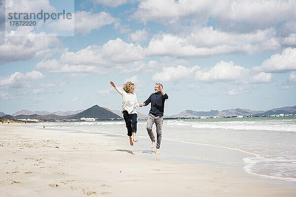 Sorgloses älteres Paar springt am Strand ans Ufer
