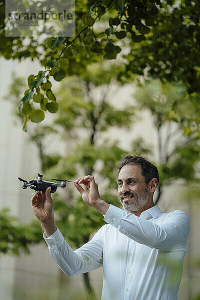 Lächelnder reifer Geschäftsmann analysiert Drohne