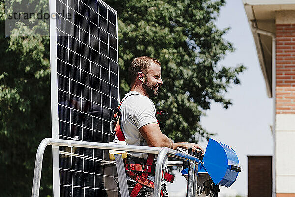 Lächelnder Elektriker mit Solarpanel auf hydraulischer Plattform