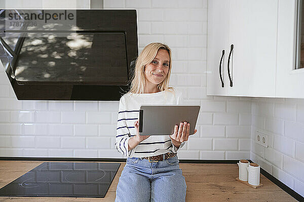 Lächelnde Frau hält zu Hause einen Tablet-PC auf der Küchentheke