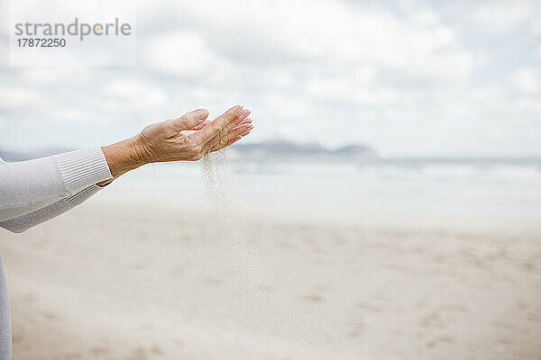 Hände einer reifen Frau  die Sand am Strand hält