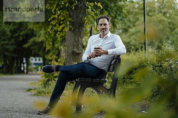 Geschäftsmann mit Smartphone sitzt auf Bank im Park