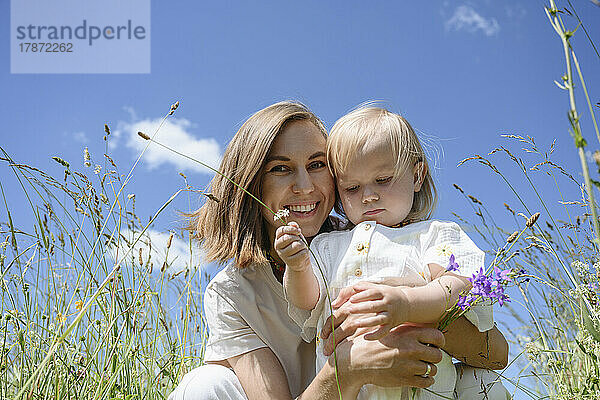 Glückliche Mutter mit Tochter  die unter dem Himmel auf dem Feld sitzt