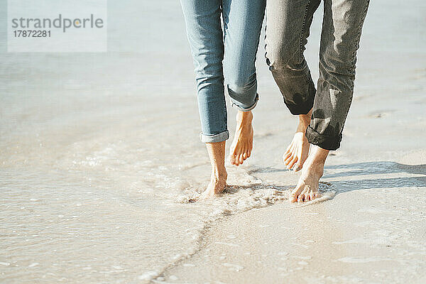Mature couple walking barefoot on shore at beach