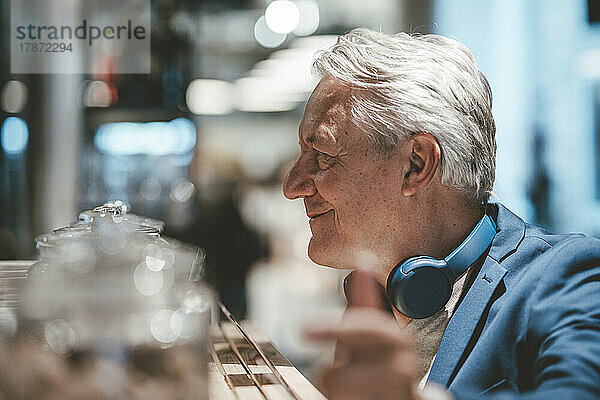 Lächelnder Geschäftsmann mit kabellosen Kopfhörern im Café