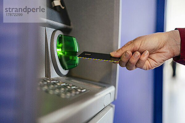 Die Hand einer Frau benutzt ihre Kreditkarte am Geldautomaten