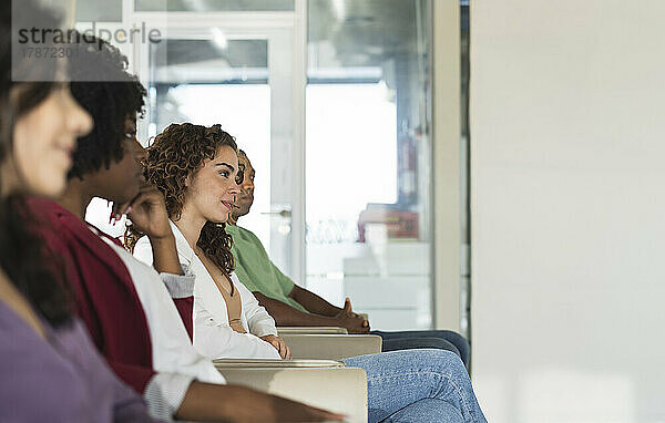 Junge Geschäftsfrau sitzt inmitten von Kollegen im Büro