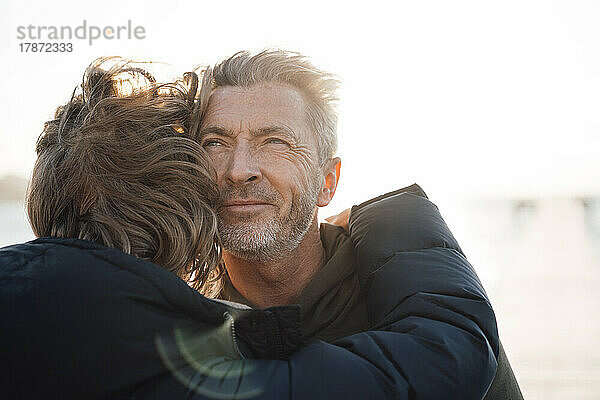 Reife blonde Frau umarmt Mann an sonnigem Tag am Pier