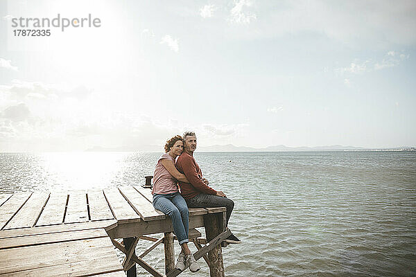 Älteres Paar sitzt auf einem Steg über dem Meer